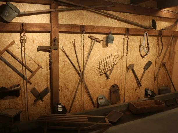 Ausstellungswand mit historischen Werkzeugen Historische landwirtschaftliche Werkzeuge hängen an einer Wand im rustikalen Ammerländer Kerzenstall.