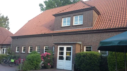 Bokeler Schule (Dörpshus) Das Bild zeigt das historische Backsteingebäude der Bokeler Schule (Dörpshus) mit einem markanten roten Ziegeldach.