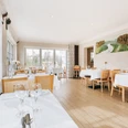 Restaurant im Laasenhof Helles Restaurant mit Holzboden, gedeckten Tischen und großen Fenstern; an der Wand ein Landschaftsgemälde.
