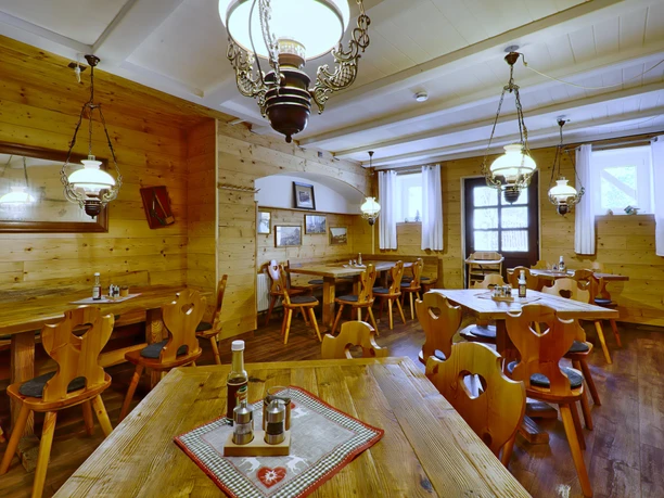 Gasthof Sennerhütte Gemütliches Restaurant mit Holzwänden und -möbeln, dekoriert mit Lampen und Bildern; Tische sind mit Gewürzen und Flaschen gedeckt.