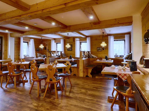 Cozy, rustic restaurant with wooden furniture, checkered tablecloths and warm lighting; empty tables and chairs, inviting atmosphere.