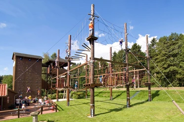 Hochseilgarten Dankern Menschen klettern gesichert auf Holzplattformen und Seilen eines Hochseilgartens unter blauem Himmel.