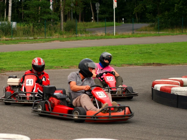 Kartsport Drei Personen fahren in roten Karts mit Helmen durch eine Kurve auf einer Outdoor-Rennstrecke.