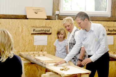 Gaudischeune bei Meutstege Erwachsene und Kinder spielen gemeinsam an einem Holzspieltisch in einer Scheune mit Naturmaterialien.