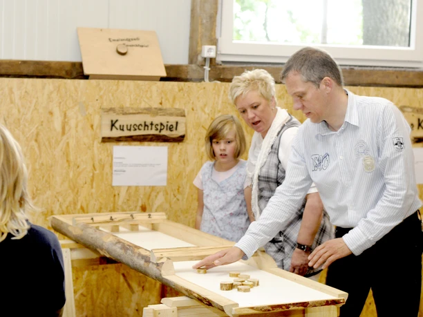 Gaudischeune bei Meutstege Erwachsene und Kinder spielen gemeinsam an einem Holzspieltisch in einer Scheune mit Naturmaterialien.