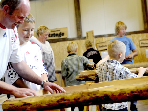 Gaudischeune bei Meutstege Erwachsene und Kinder lachen gemeinsam beim Spielen an Holzkonstruktionen in einer Scheune.