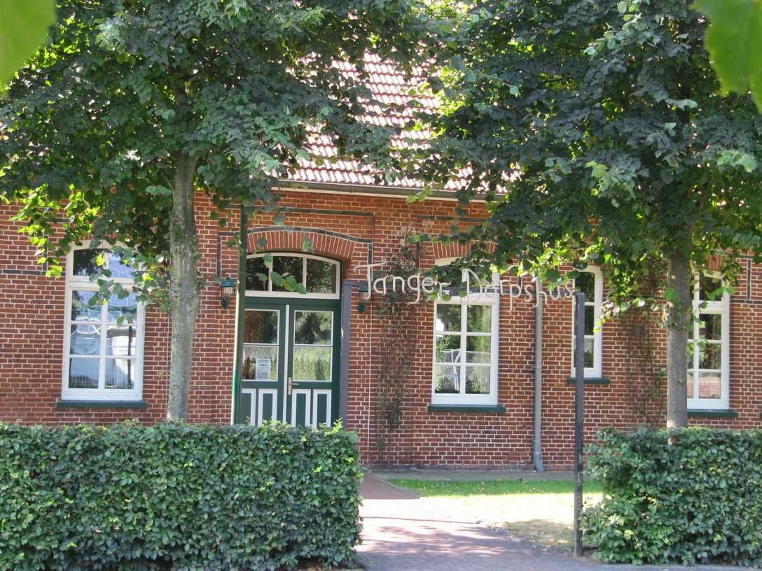 Dörpshus in Tange Vorm Dörpshus in Tange stehen zwei große, schattenspendende Bäume vor einer roten Backsteinfassade.