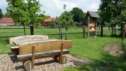 Rastplatz Hengstforde-Apen Ein ruhiger Rastplatz mit einer Holzbänken-Garnitur des OBV Hengstforde, grüner Wiese und Insektenhotel.