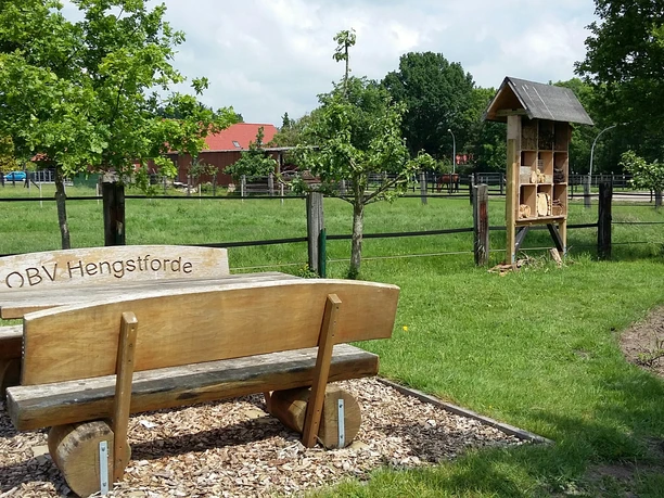 Rastplatz Hengstforde-Apen Ein ruhiger Rastplatz mit einer Holzbänken-Garnitur des OBV Hengstforde, grüner Wiese und Insektenhotel.