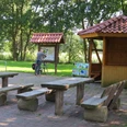 Rastplatz Am Drakamp Holzpicknicktische stehen auf gepflastertem Gelände, flankiert von einer Info-Tafel und einem Radfahrer.