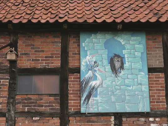 Großes Wandgemälde auf einem Ziegelbau zeigt zwei Reiher mit Krone und eine Eule in einem Gemäuer.