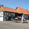 Alte Schule Wietersheim Fachwerkgebäude mit rotem Ziegeldach in Dorfumgebung, mehrere Menschen mit Fahrrädern im Vordergrund.
