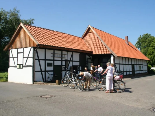 Alte Schule Wietersheim Fachwerkgebäude mit rotem Ziegeldach in Dorfumgebung, mehrere Menschen mit Fahrrädern im Vordergrund.