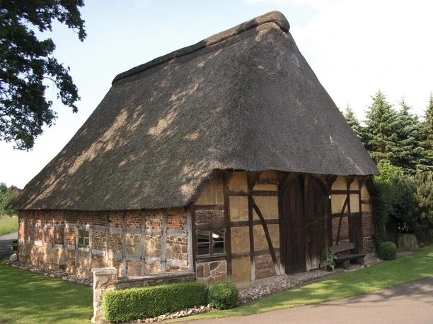 Handwerks-Dorf Frotheim Reetgedecktes Fachwerkhaus in ländlicher Umgebung, umgeben von Bäumen und einer Wiese.