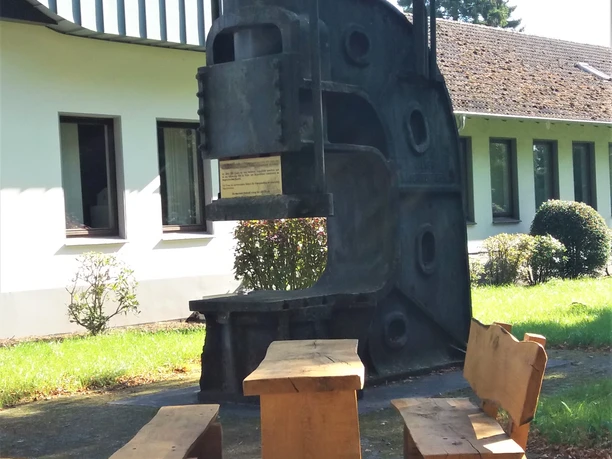 Schmiedehammer am Rastplatz Auf dem Bild ist ein historischer Schmiedehammer zu sehen, der als Rastplatz mit Sitzbänken dient.