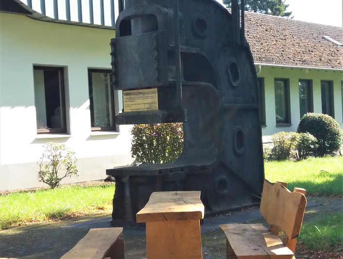 Schmiedehammer am Rastplatz Auf dem Bild ist ein historischer Schmiedehammer zu sehen, der als Rastplatz mit Sitzbänken dient.