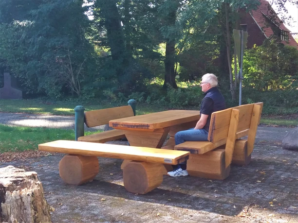 Sitzgruppe am Stahlwerk Eine Sitzgruppe aus massiven Holzblöcken mit Bänken und Tisch steht harmonisch im Grünen. Eine Person sitzt auf einer Bank und genießt die Natur.