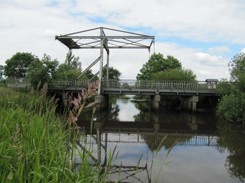 Alte Staaßenbrücke Eine alte, metallene Zugbrücke über einem ruhigen Kanal, umgeben von üppigem Grün.