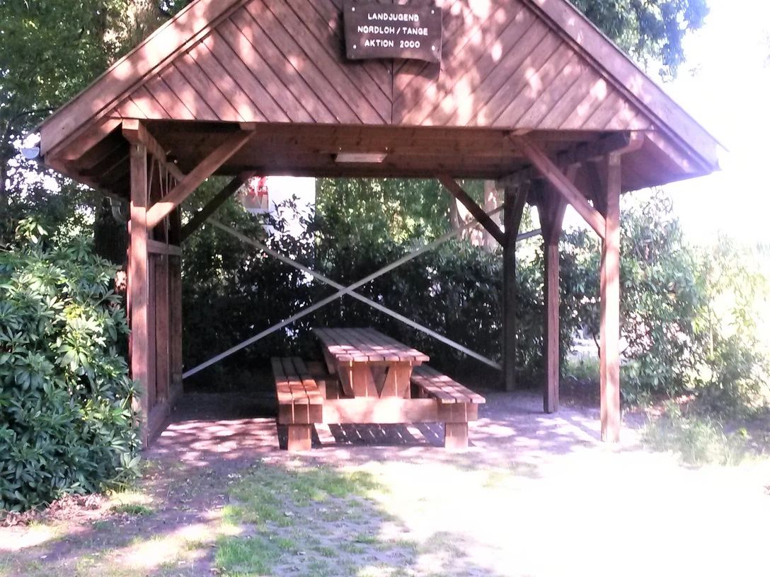 Rastplatz Nordloh Ein hölzerner Pavillon bietet Schutz und beherbergt eine rustikale Sitzgruppe unter knorrigen Bäumen.