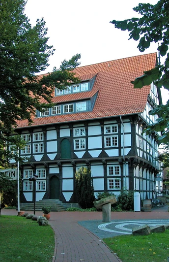 Abtei Wunstorf Fachwerkhaus der Abtei Wunstorf mit rotem Dach, umgeben von Laubbäumen, blauem Himmel im Hintergrund.