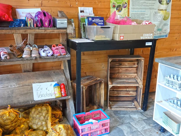 Eierhütte Hof Engelken Holzregal mit Kinderschuhen und Helmen, daneben Tisch und Regale mit Eierkartons in einer Verkaufshütte