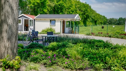 Martins Fietzensaloon Kleines Gartenhäuschen mit Terrasse, Tisch, Stühlen und Fahrrad vor blühenden Sträuchern im Grünen.