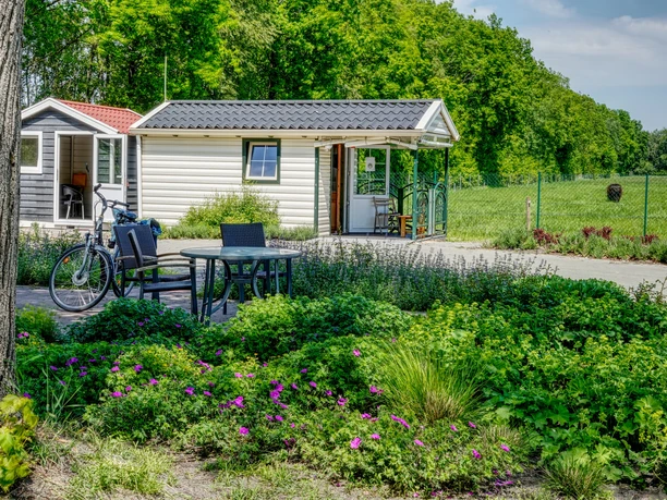 Martins Fietzensaloon Kleines Gartenhäuschen mit Terrasse, Tisch, Stühlen und Fahrrad vor blühenden Sträuchern im Grünen.