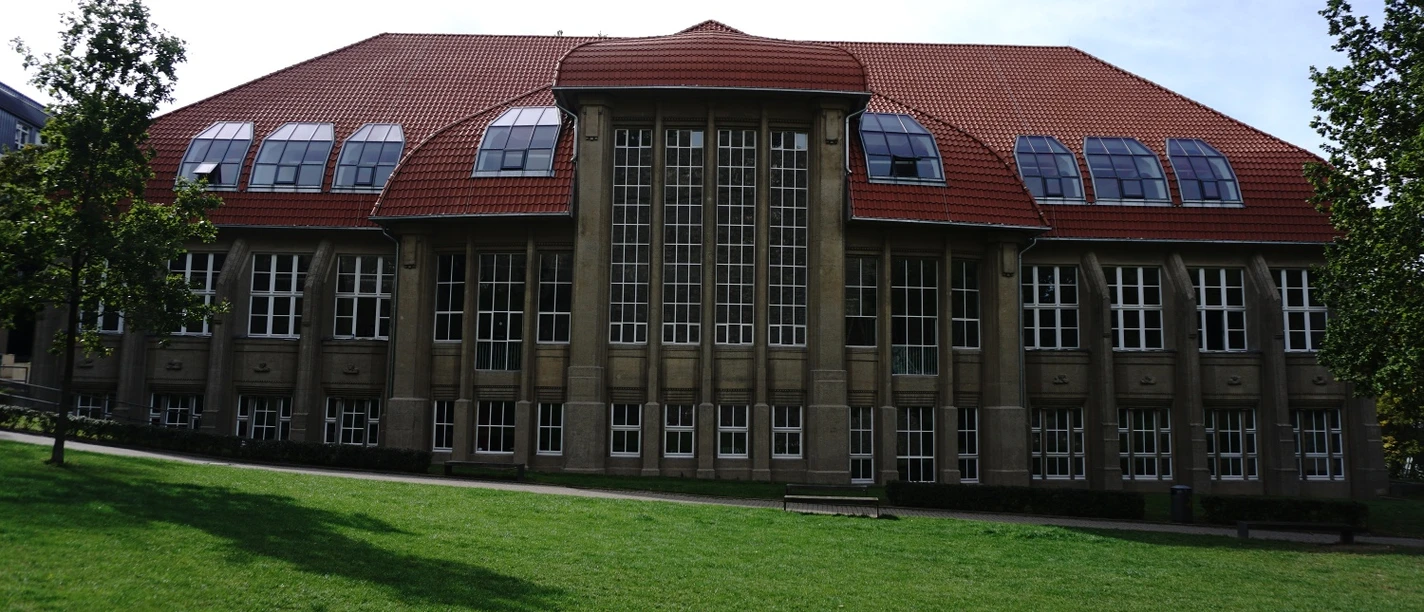 Musik- und Kunstschule Bielefeld Historisches Backsteingebäude mit gewölbtem Dach und großen Fenstern vor grüner Wiese.