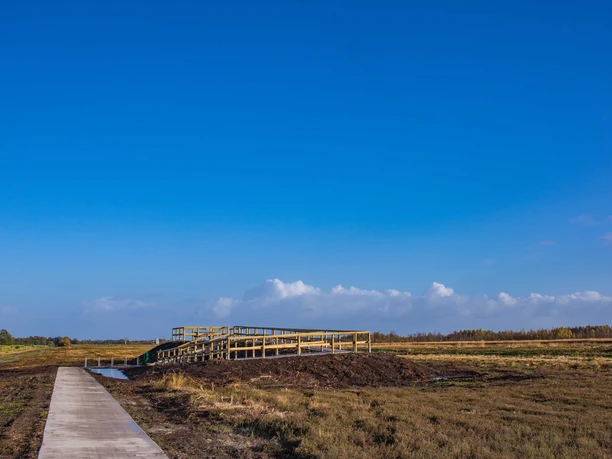 Aussichtspunkt Fehndorfer Moor Holzplattform mit Geländern im weiten Moorgebiet unter blauem Himmel mit vereinzelten Wolken.