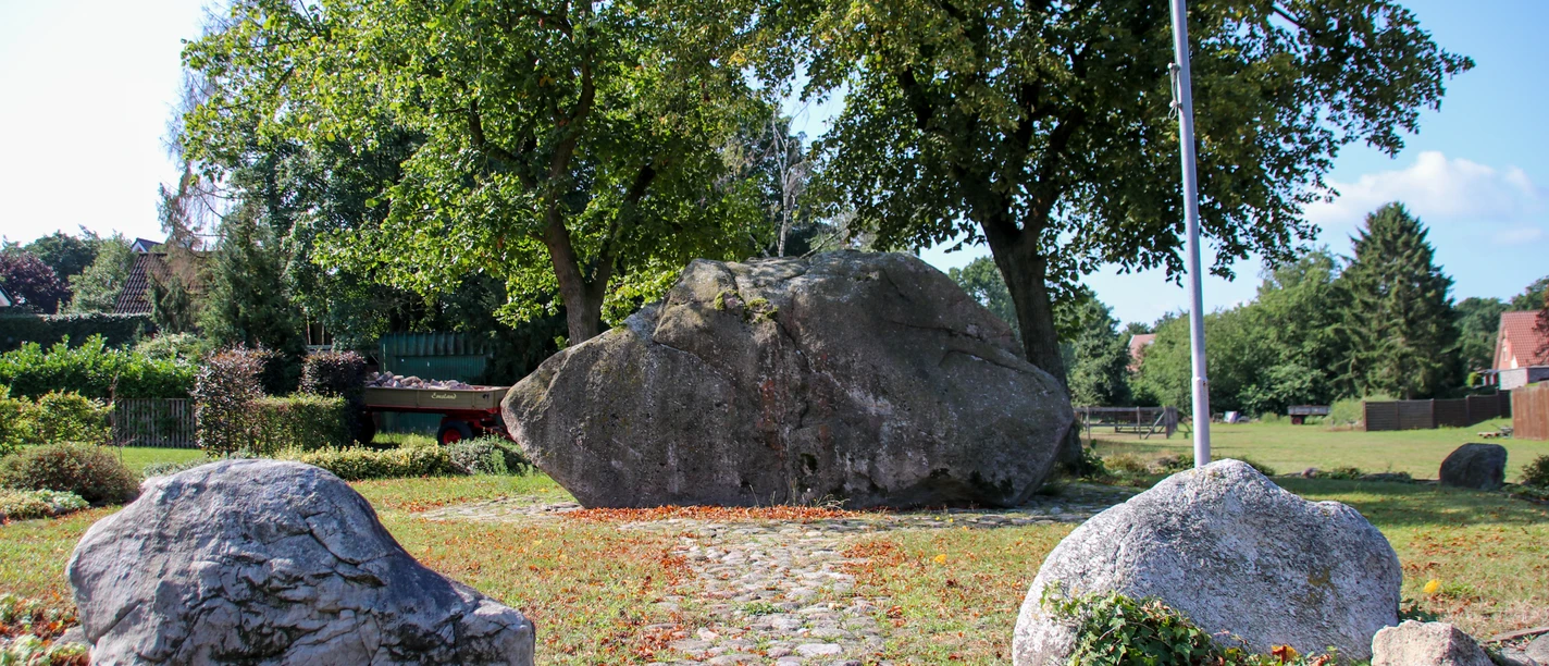 Opferstein Börger Großer Findling im Grünen, von Bäumen umgeben, mit gepflastertem Weg und weiteren Steinen im Vordergrund.