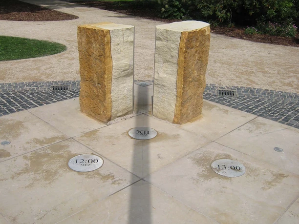 Schattenwurf der Sonnenuhr Steinhude Zwei aufrecht stehende Steinsäulen einer Sonnenuhr werfen einen Schatten auf den darunter liegenden Boden.