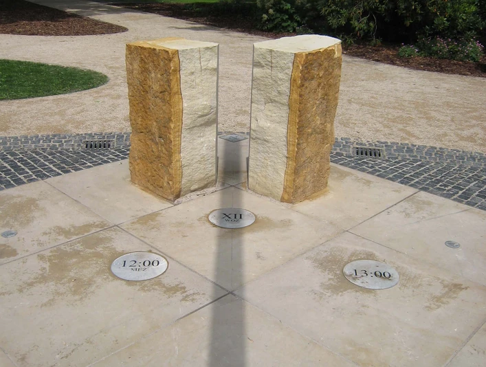 Schattenwurf der Sonnenuhr Steinhude Zwei aufrecht stehende Steinsäulen einer Sonnenuhr werfen einen Schatten auf den darunter liegenden Boden.