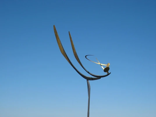 Eine elegante Windskulptur erhebt sich vor dem Steinhuder Meer, mit Wilhelmstein im Hintergrund.