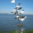 Undines Traum Eine moderne, silberne Skulptur eines Segels mit Wellen steht im klaren Wasser eines Sees.