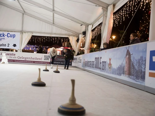 01-eisstockschiessen Menschen spielen abends unter Lichterketten Eisstockschießen auf der überdachten Bahn in Bad Zwischenahn.