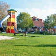 Abenteuerspielplatz Greetsiel Kinder spielen auf einer großen Wiese mit Holzschaukeln, Rutsche und rot-gelbem Aussichtsturm in Greetsiel.