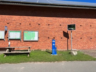 Das Bild zeigt eine blaue Lufttankstation vor einer roten Backsteinmauer mit Infotafeln und Spiegel.