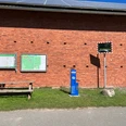 Das Bild zeigt eine blaue Lufttankstation vor einer roten Backsteinmauer mit Infotafeln und Spiegel.