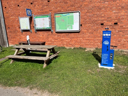 Lufttankstelle Wienbergen Fahrrad-Lufttankstelle neben Picknicktisch vor einer Ziegelwand mit Informationsschildern.