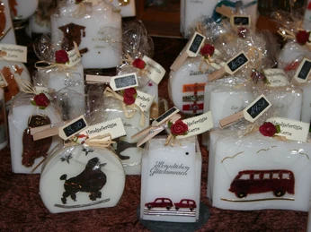 handwerkshuette23 Verschieden geformte, handgefertigte Kerzen mit Motiven und Schleifendekor auf Verkaufsstand.