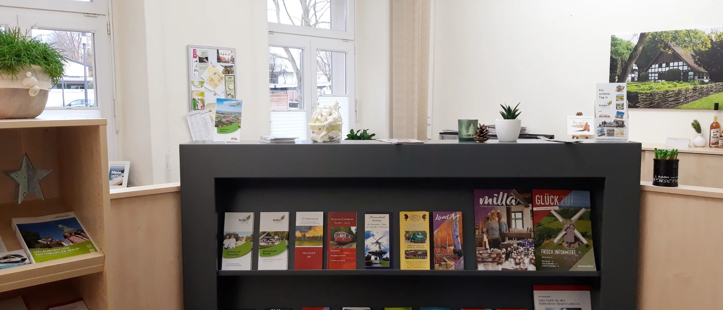 Innenraum einer Tourist-Information mit Prospektständer, vielen Broschüren und ans Fenster grenzendem Tisch.