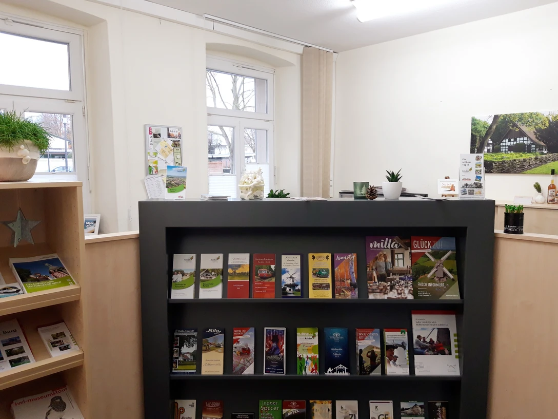 Touristinfo Rahden Innenraum einer Tourist-Information mit Prospektständer, vielen Broschüren und ans Fenster grenzendem Tisch.