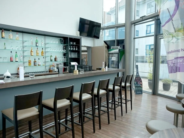 Cocktailbar Moderne Bar mit hohen Stühlen, gut bestückt mit Spirituosen, Glaswand zur Terrasse, helle Atmosphäre.