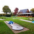 Ein weitläufiger Minigolfplatz mit verschiedenen Bahnen, Bänken und einem hölzernen Pavillon im Hintergrund.