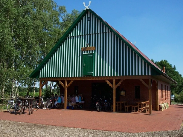 Backsteingebäude mit grünen Fensterläden und Satteldach, umgeben von Fahrrädern und Bäumen.