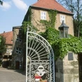Schloss Petershagen Hohes, von Efeu bewachsenes Schlossgebäude mit rotem Ziegeldach und verziertem Eisentor im Vordergrund.