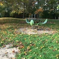 Ein grünes, schiffsförmiges Klettergerät auf einem Laubbedeckten Spielplatz an einem Herbsttag.