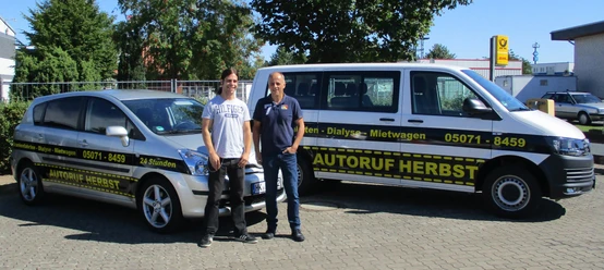 autoservice-herbst-taxi-fahrservice-buchholz-aller Zwei lächelnde Männer stehen vor zwei Autos von Autoruf Herbst in Buchholz Aller.