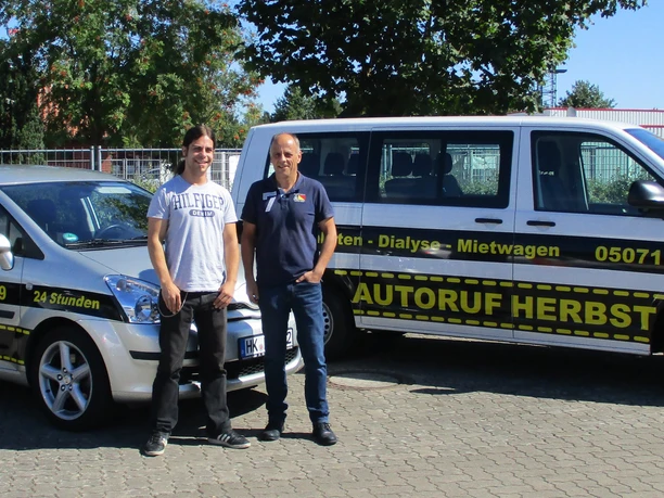 autoservice-herbst-taxi-fahrservice-buchholz-aller Zwei lächelnde Männer stehen vor zwei Autos von Autoruf Herbst in Buchholz Aller.