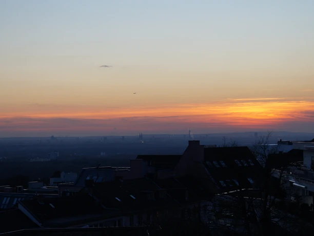 abendlicher Ausblick von Schloss Bensberg Ein ruhiger Sonnenuntergang über einer Stadtlandschaft mit silhouettierten Dächern im Vordergrund.